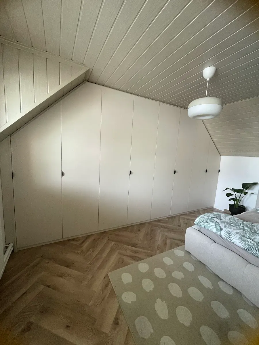 Podkrovná spálňa so svetlými skriňami na mieru pod šikminou pozdĺž celej steny.